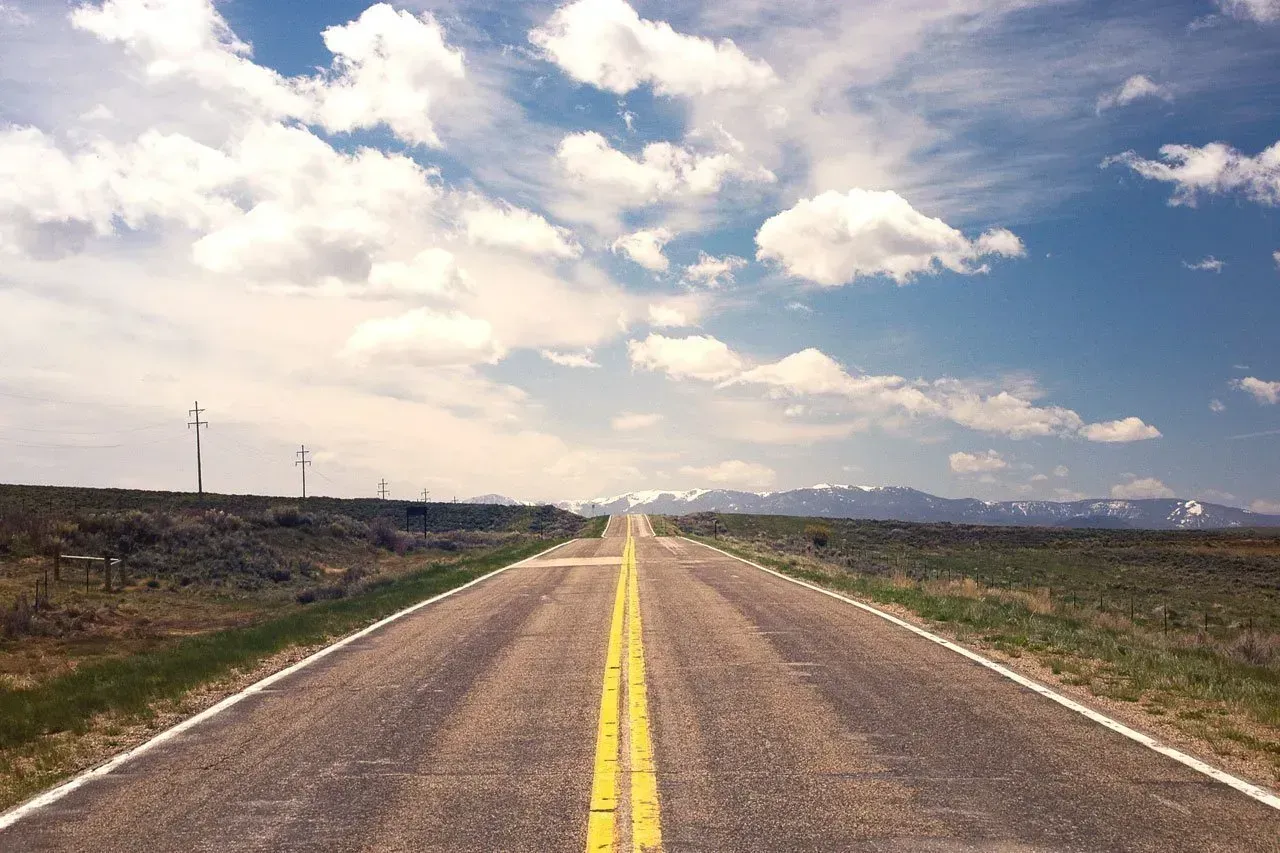 A road that is going through a field with mountains in the background.