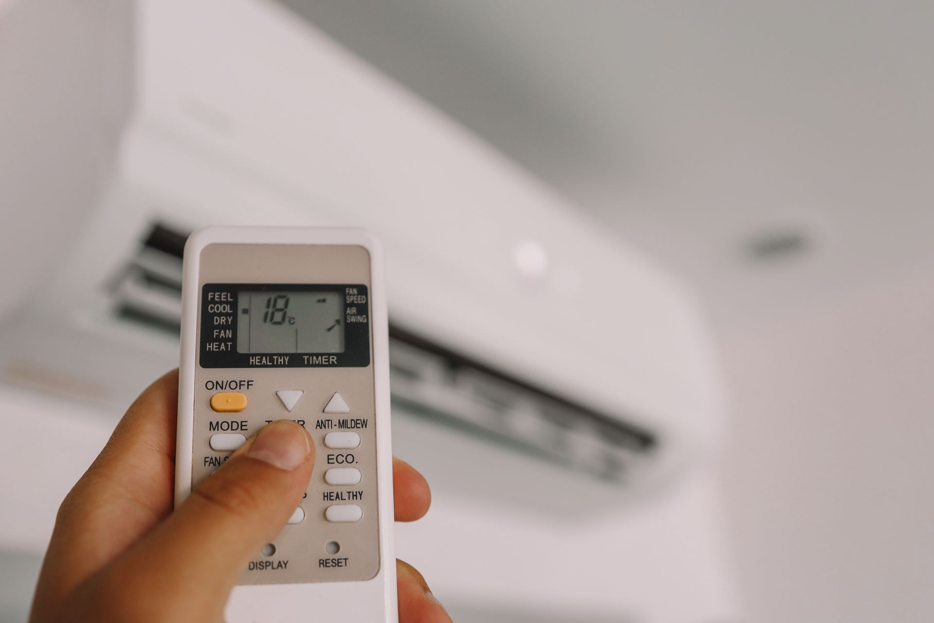 Hand holding an AC remote pointed at a wall-mounted air conditioner