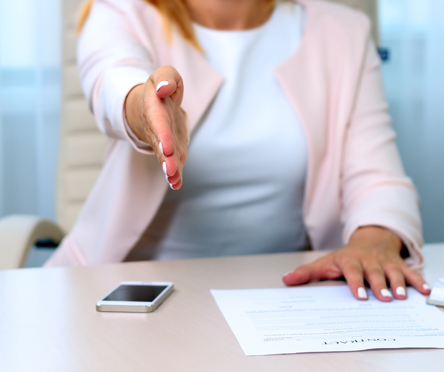 A woman is sitting at a desk shaking hands with another woman.