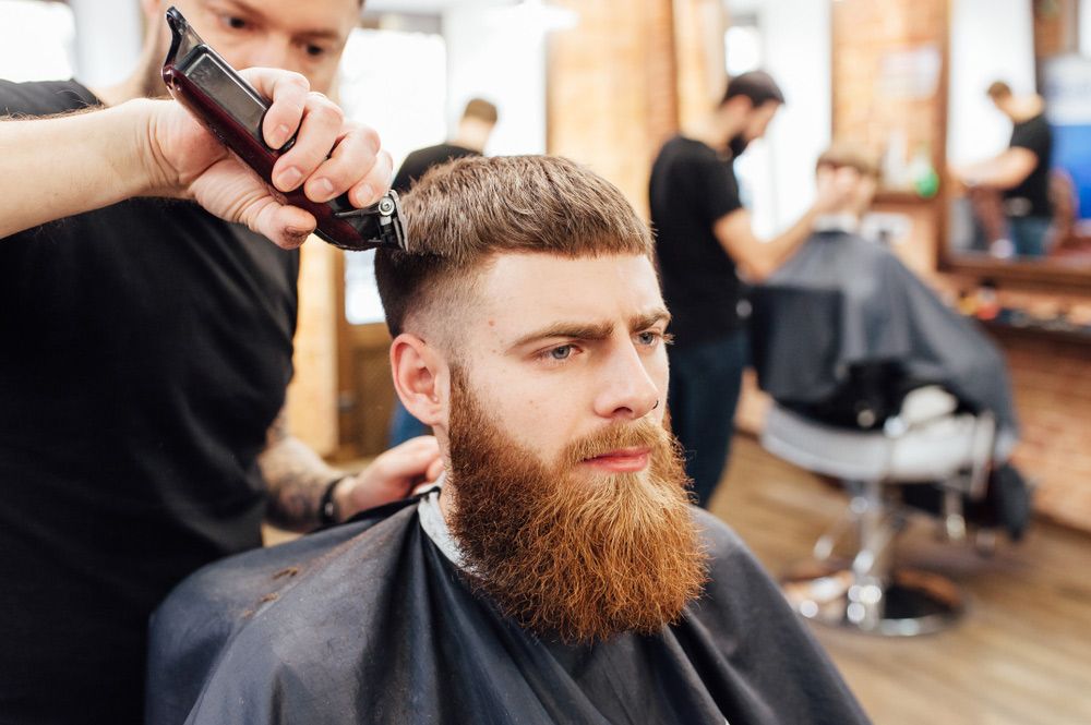 A Man With A Beard Is Getting His Hair Cut By A Barber In A Barber Shop — Bermann Barbershop In Casey, ACT