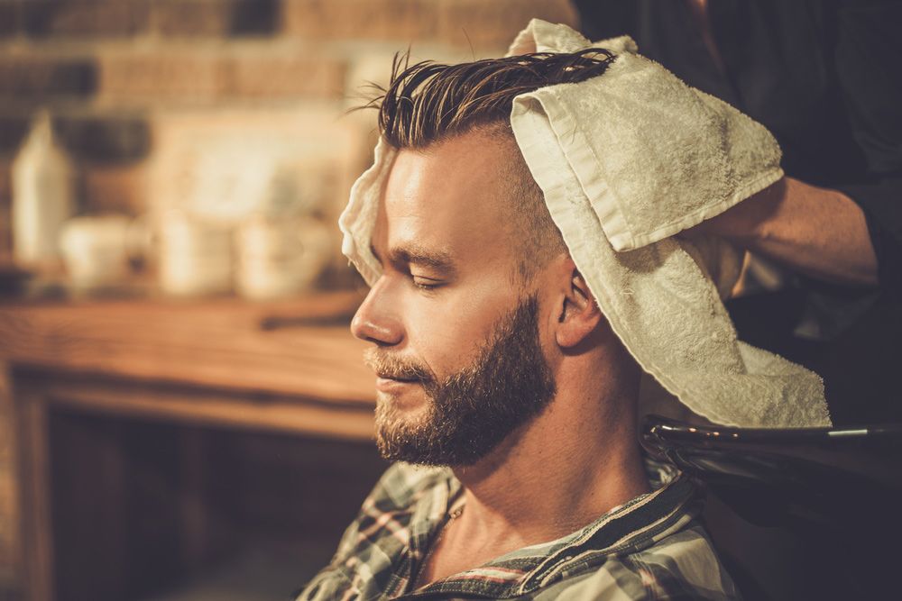A Man With A Beard Is Getting His Hair Washed By A Barber — Bermann Barbershop In Casey, ACT