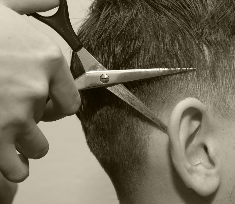 Hairdresser Cutting Hair With Scissors Near a Person's Ear — Bermann Barbershop in Casey, ACT