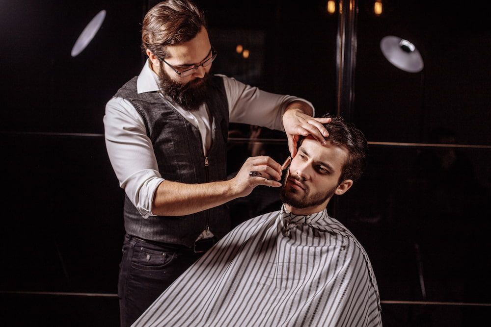 Barber Shaves Client's Face With Straight Razor in Dimly Lit Barber Shop — Bermann Barbershop in Ngunnawal, ACT