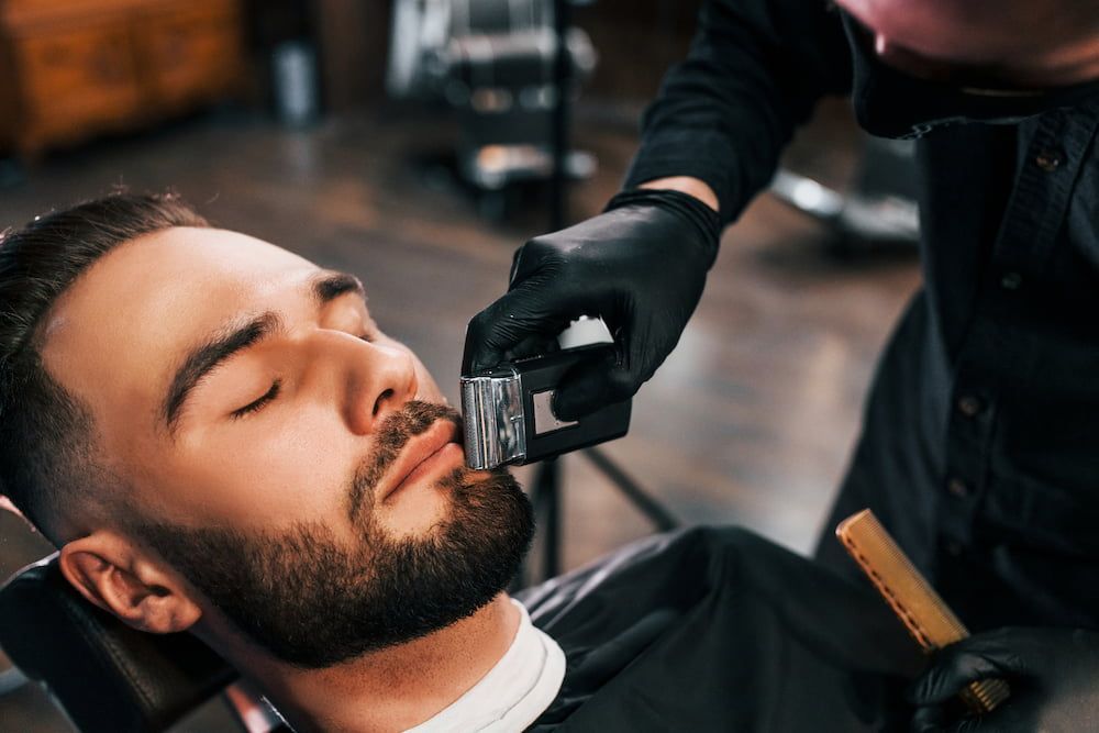 Man Getting Beard Shaved by a Barber Wearing Black Gloves in a Barbershop — Bermann Barbershop in Nicholls, ACT