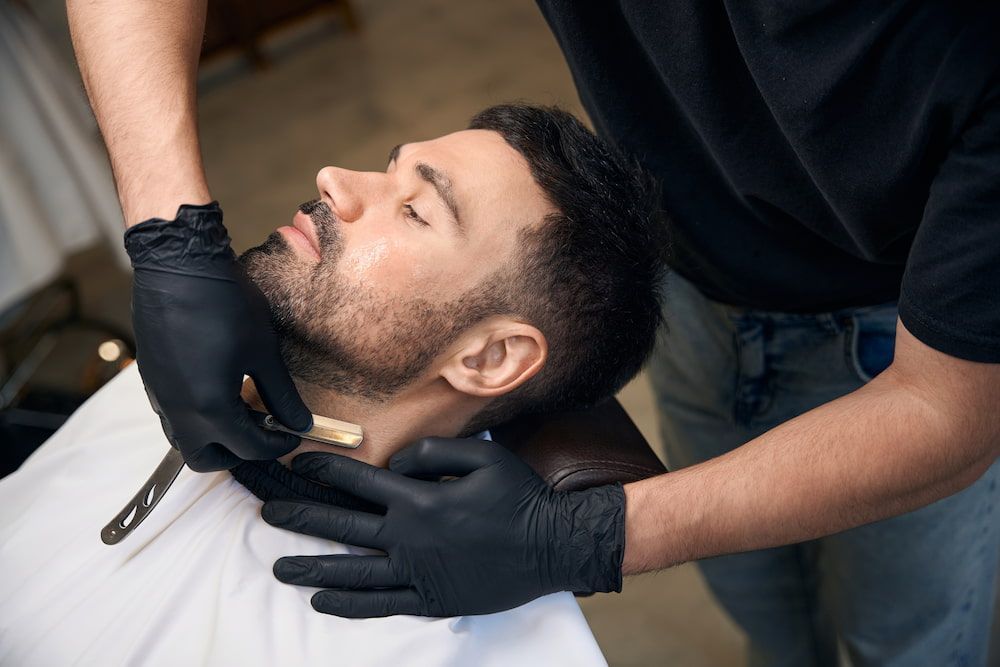 Barber Shaves a Man's Neck With a Straight Razor; Both Are Wearing Black Gloves — Bermann Barbershop in Ngunnawal, ACT