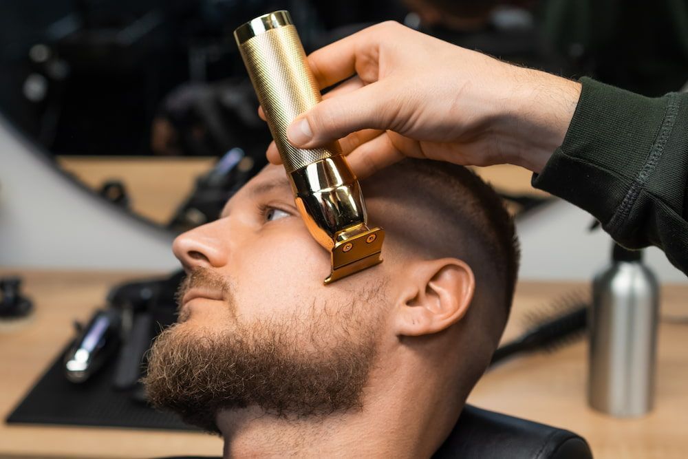 Barber Trimming a Man's Beard With a Gold Trimmer in a Barbershop — Bermann Barbershop in Gungahlin, ACT