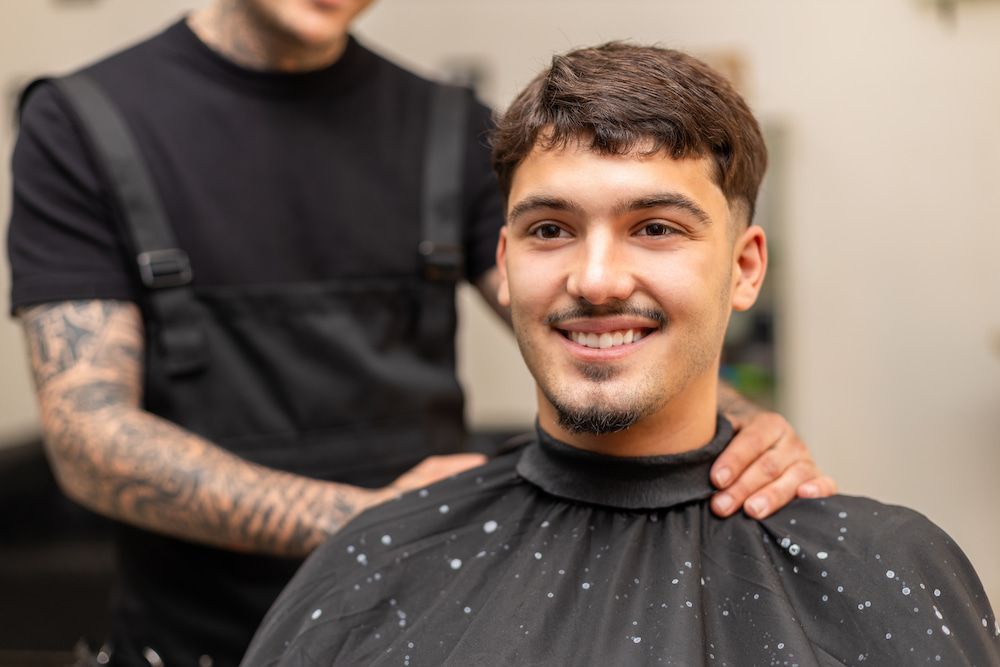 Man Smiles After a Haircut in a Salon. Stylist in Black Overalls Has Hand on Shoulder — Bermann Barbershop in Gungahlin, ACT