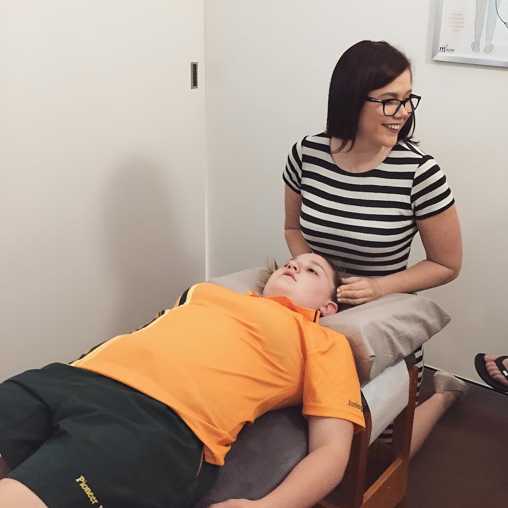 A Woman In A Striped Shirt Sits Next To A Child Laying On A Table — Grays Chiropractic Centre In Eimeo, QLD