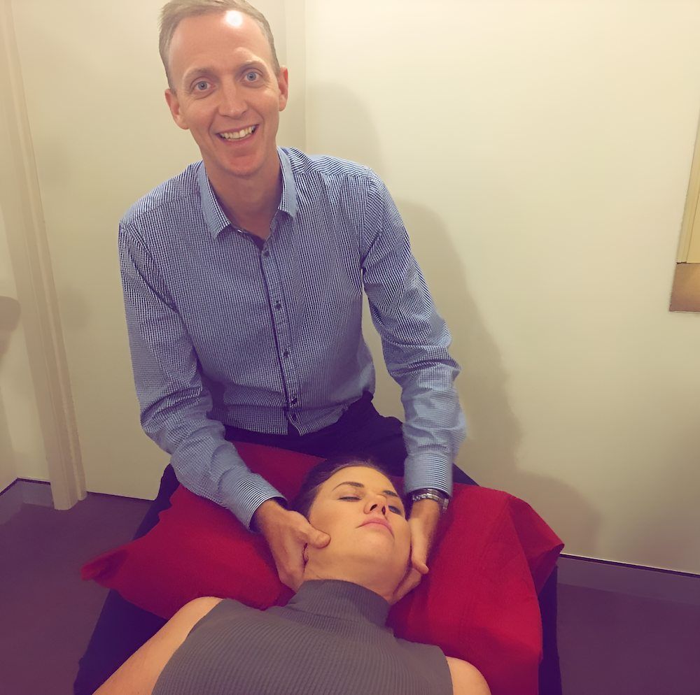 A Man Is Giving A Woman A Massage On A Red Pillow — Grays Chiropractic Centre In Beaconsfield, QLD