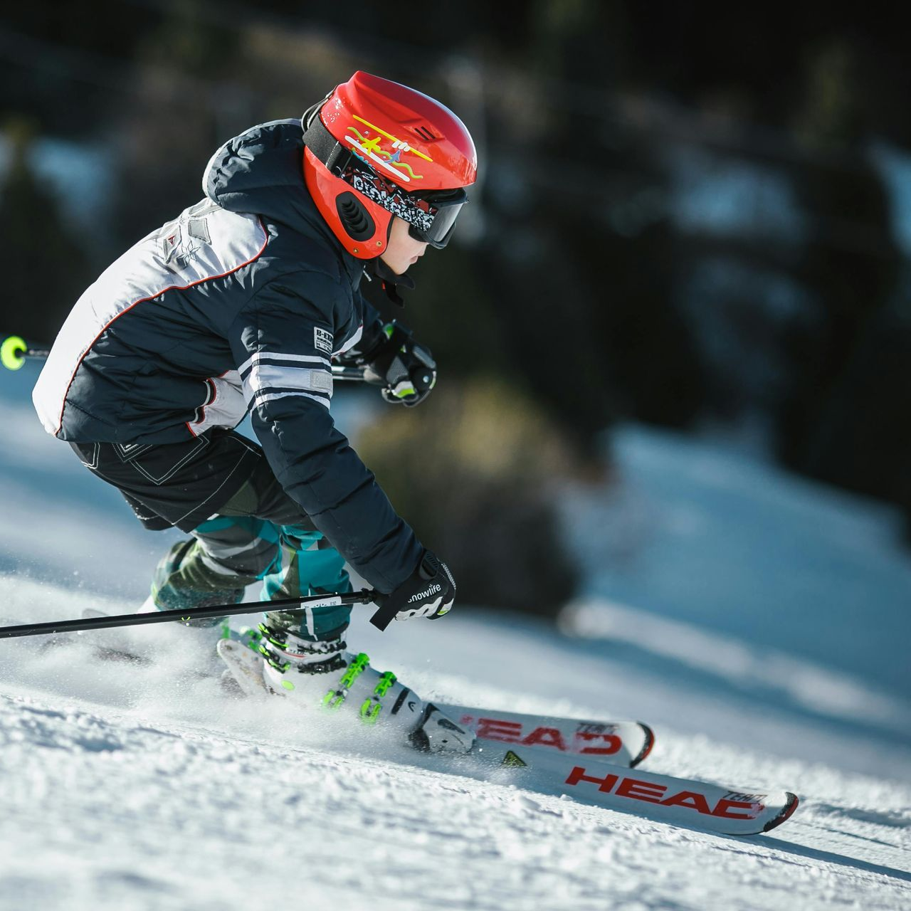 Young skier in red helmet carves down snowy slope.