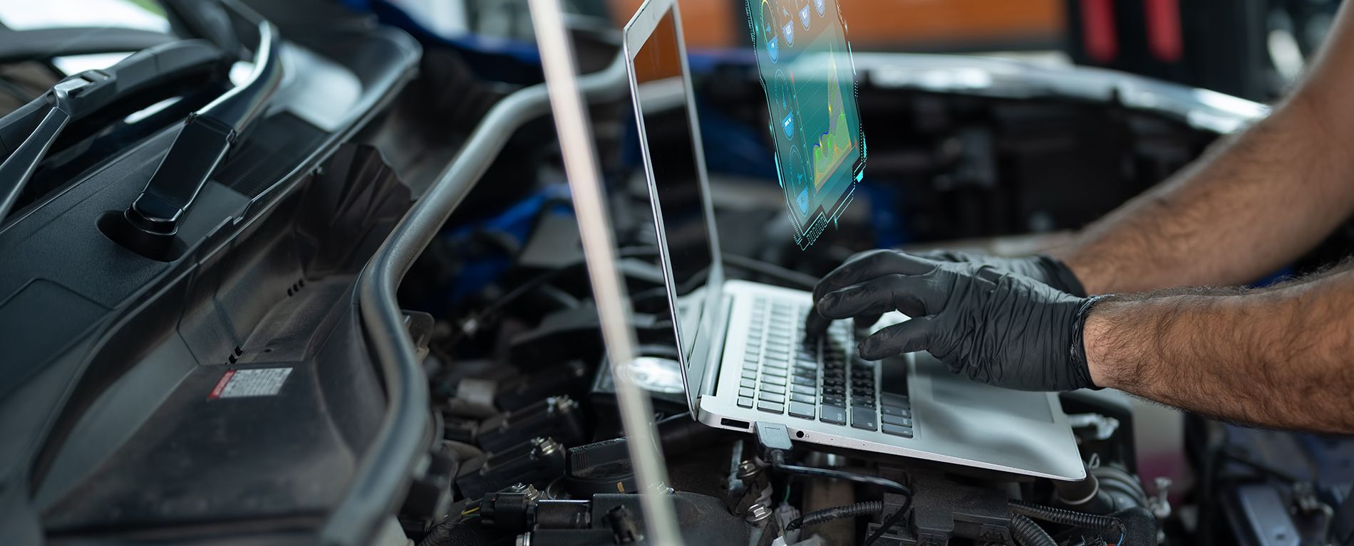 Mechanic using a laptop to diagnose a car engine. The mechanic wears gloves.