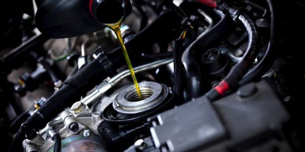 A close up of a person pouring oil into a car engine.