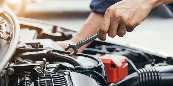 A man is working on the engine of a car with a wrench.