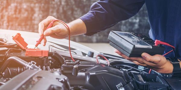 A mechanic is working on a car with a multimeter.