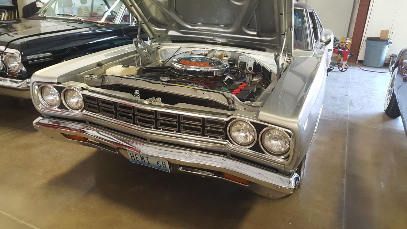 A silver car with the hood up is parked in a garage.