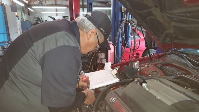A man is looking under the hood of a car in a garage.