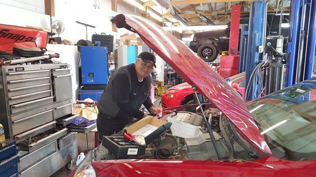 A man is working on a red car in a garage with the hood open.