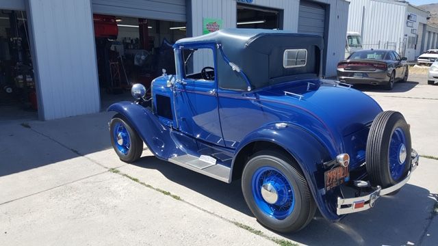 An old blue car is parked in front of a garage.