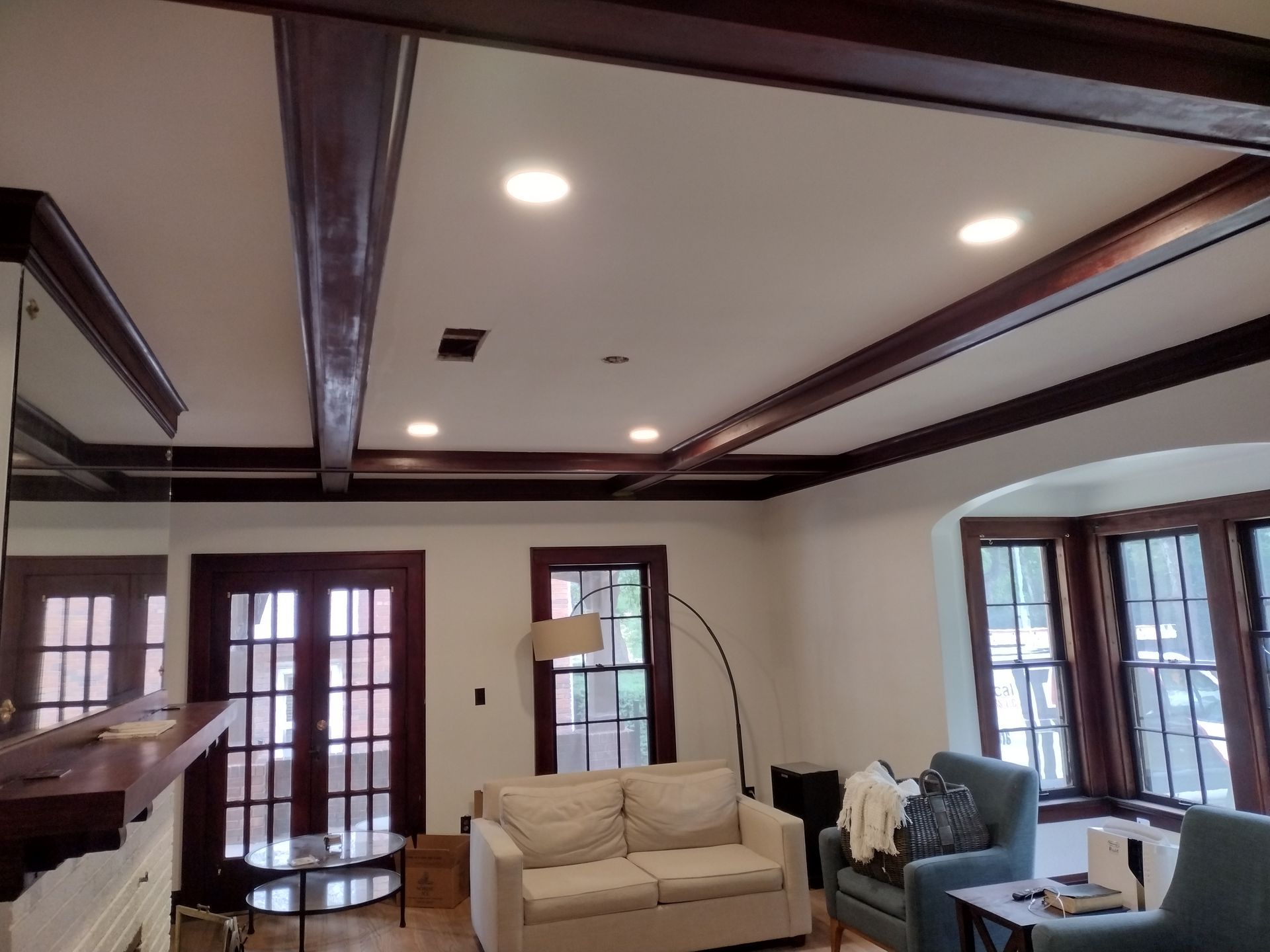 Living room with dark wood beams on the ceiling, cream walls, beige couch, and a bay window.