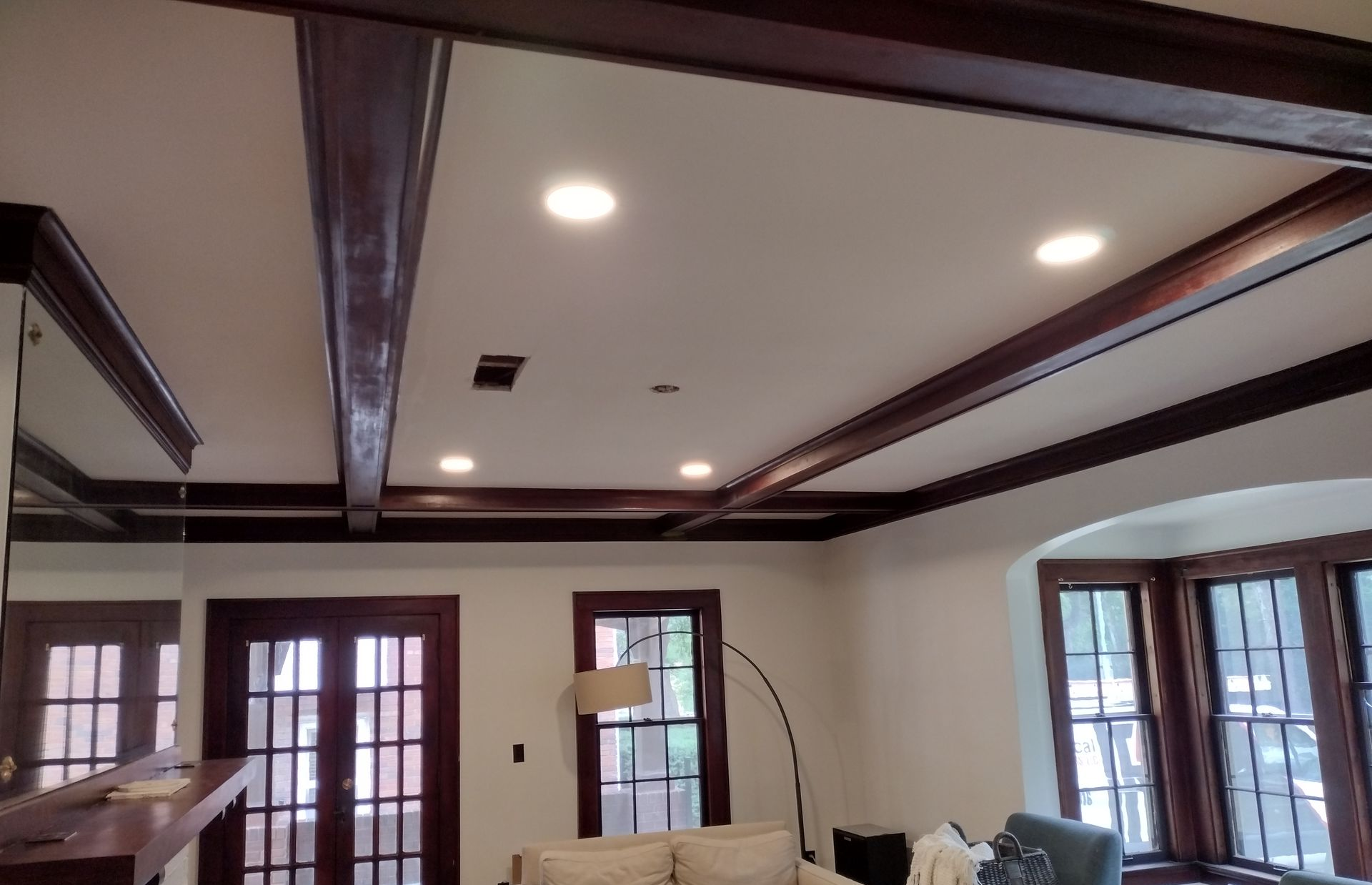 Living room with white walls, dark wood beams, and recessed lighting; includes doors and windows.