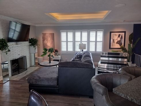 Living room with dark gray sectional, fireplace, white shutters, and artwork.