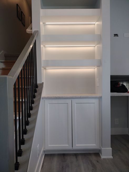 Built-in white shelving unit with LED lighting, cabinets below, next to a staircase.
