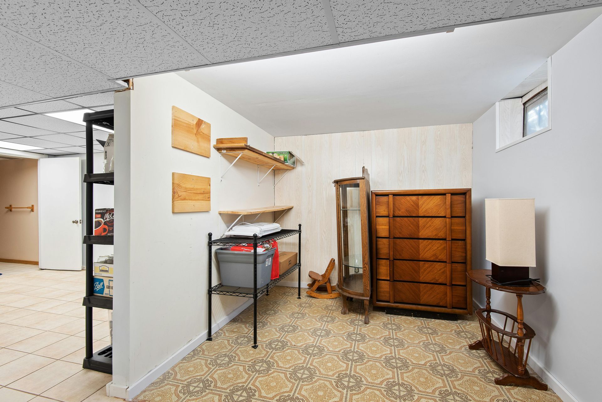 Basement room with shelving, storage cabinet, and decorative items. Beige floral carpet and paneled walls.