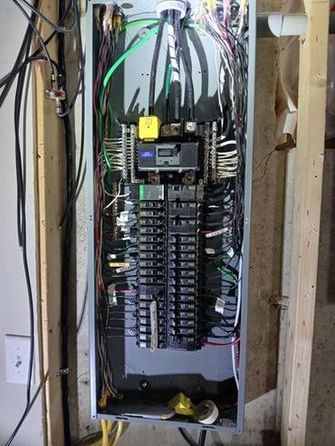 Electrical panel with many wires and breakers in a wooden frame, indoors.