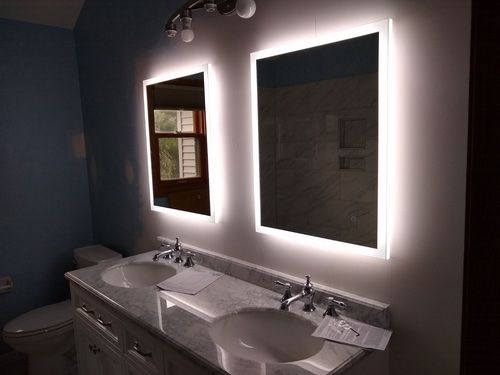 Two illuminated mirrors above a double sink vanity in a bathroom; blue walls.