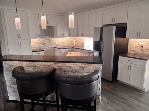Modern kitchen with white cabinets, black countertops, stone accent wall, bar stools, and pendant lights.