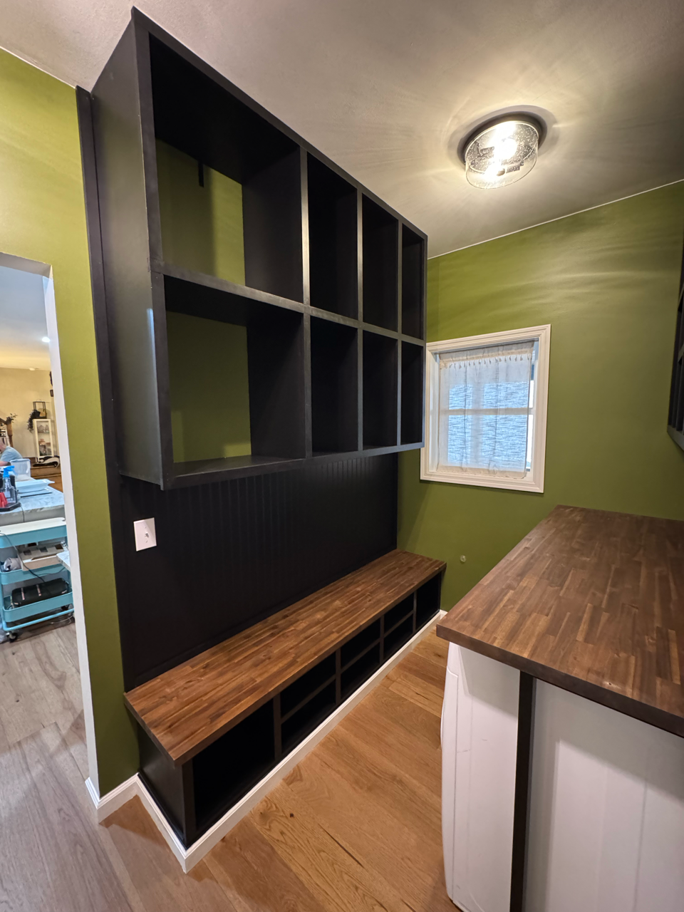 A mudroom featuring black built-in storage cubbies, a dark wood bench, and olive green walls with a wood-topped counter.