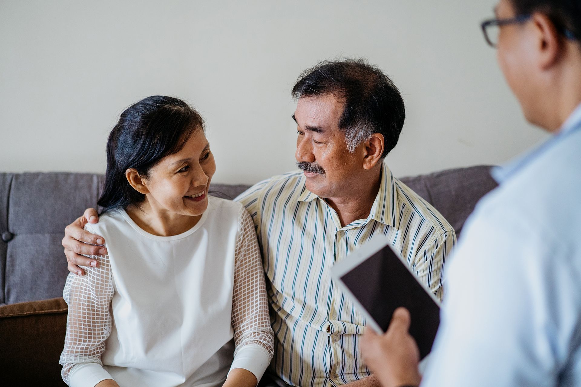 An elderly couple is sitting on a couch talking to a doctor.