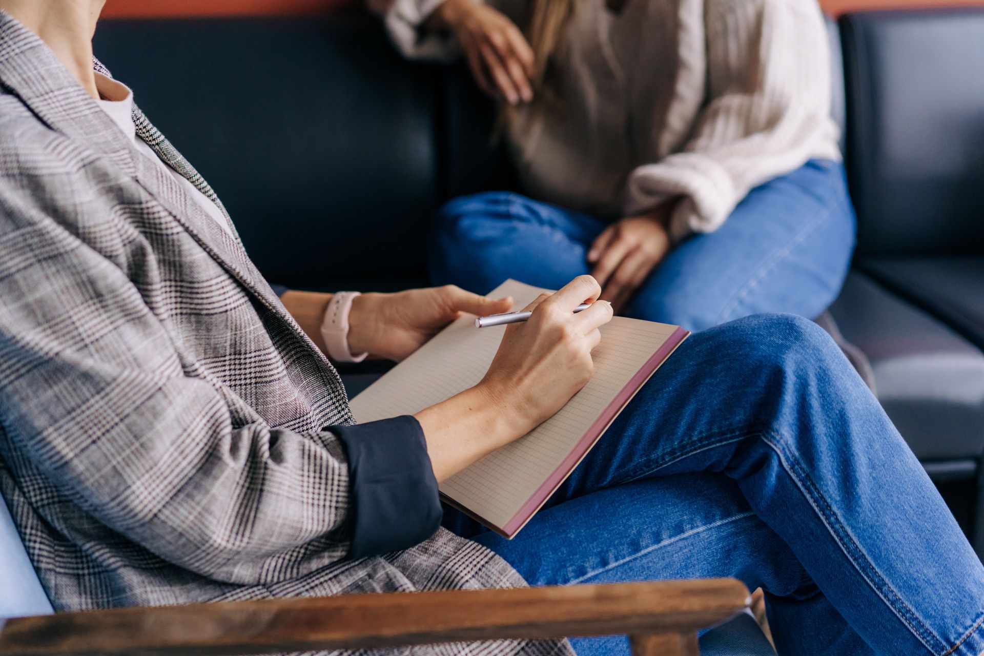 Close-up of a psychologist's hands writing down notes about a patient in a notebook.