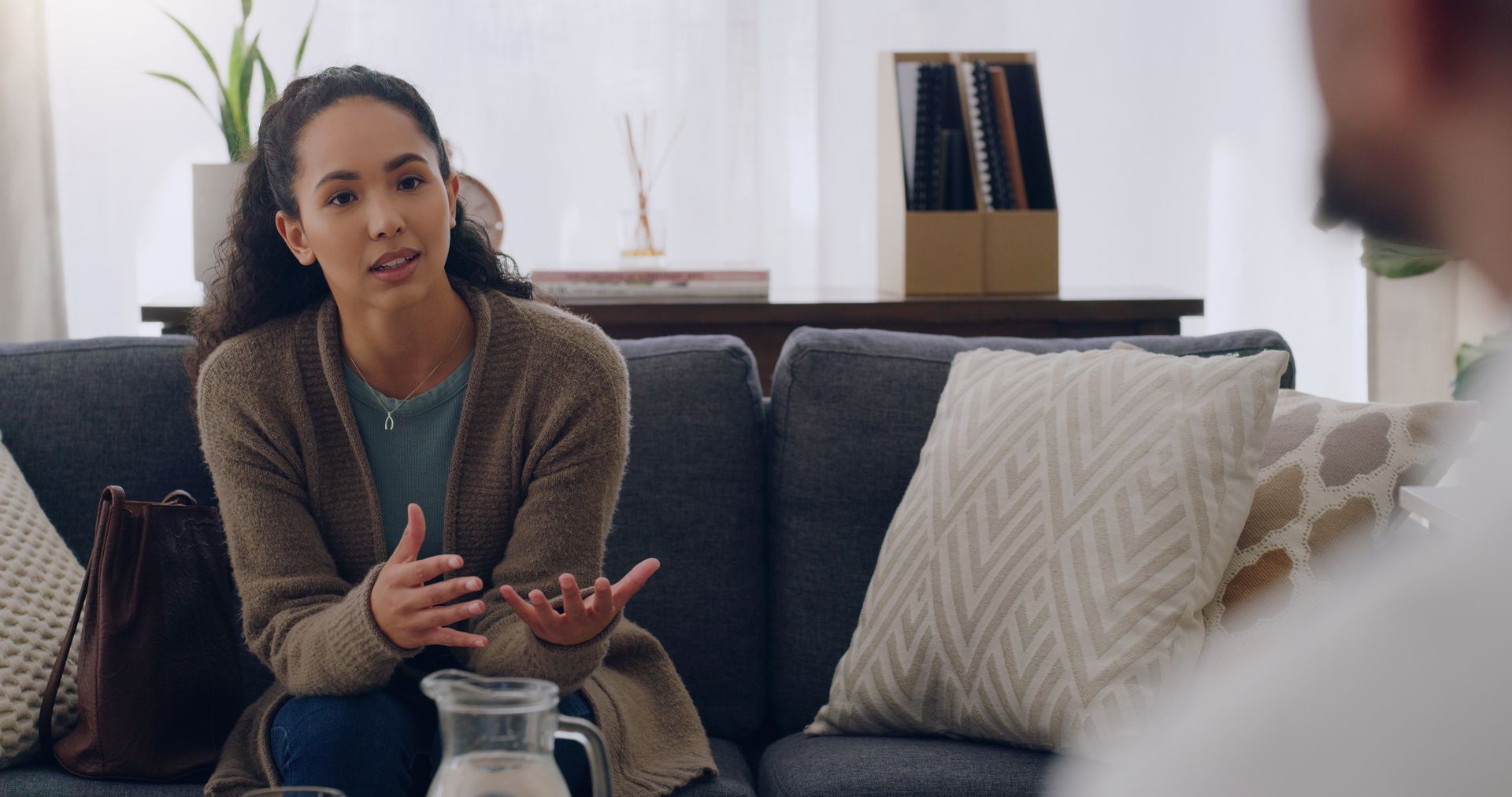 A woman seated on a sofa while talking to her psychologist, for anxiety counselling services.
