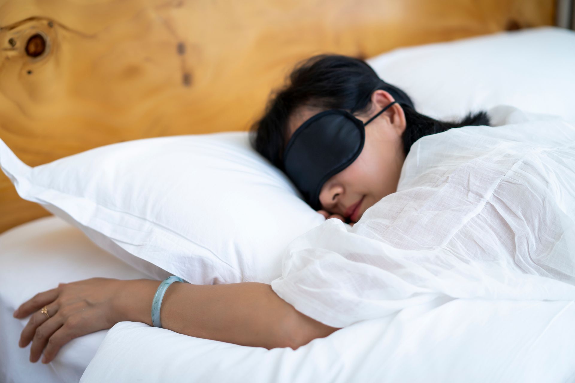 A woman wearing a sleep mask is sleeping on a bed.