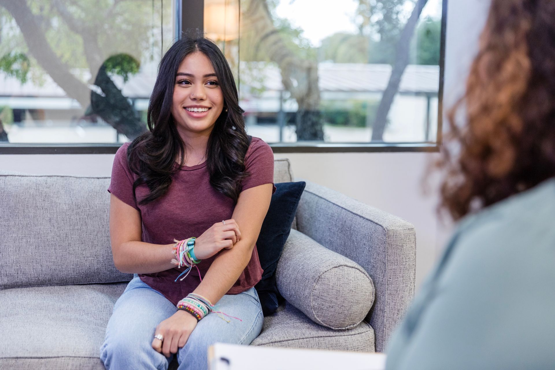 A woman is sitting on a couch talking to another woman.