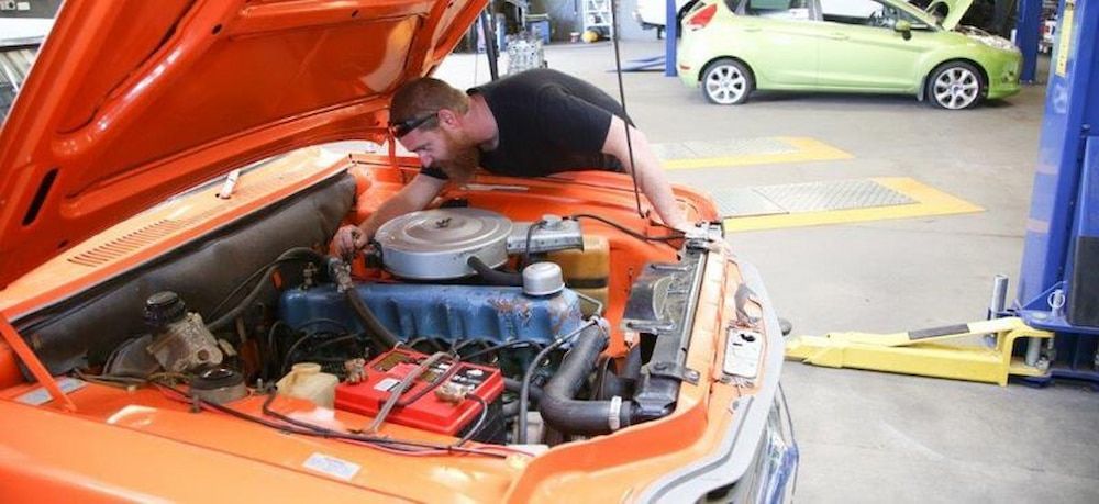 A Man Is Working On The Engine Of An Orange Car — Cam Duffy Autos In Atherton, QLD