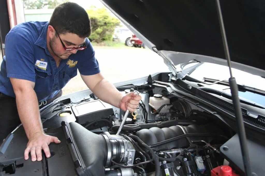 A Man In A Blue Shirt Is Working On The Engine Of A Car — Cam Duffy Autos In Atherton, QLD