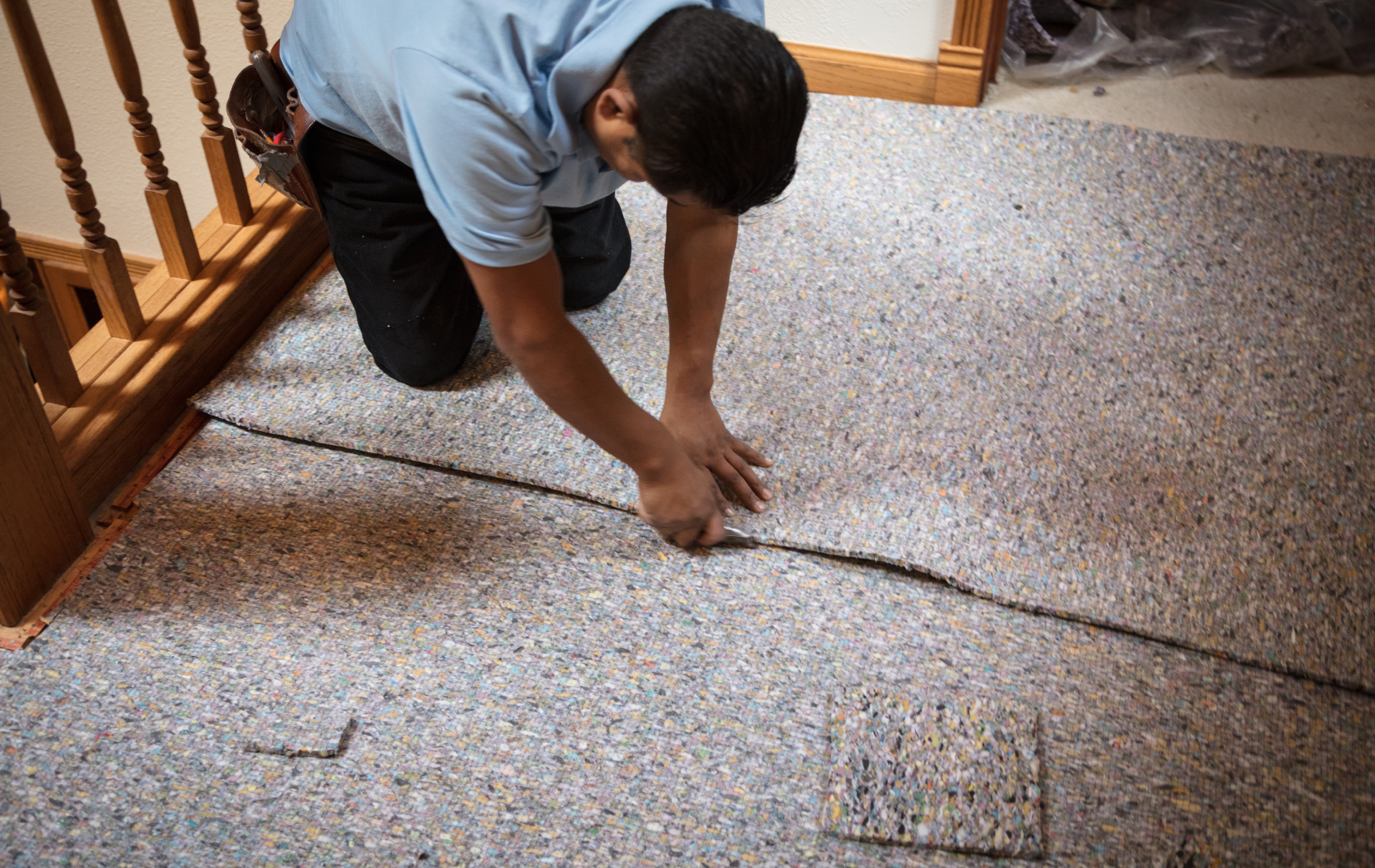 A man is kneeling down and cutting a piece of carpet.