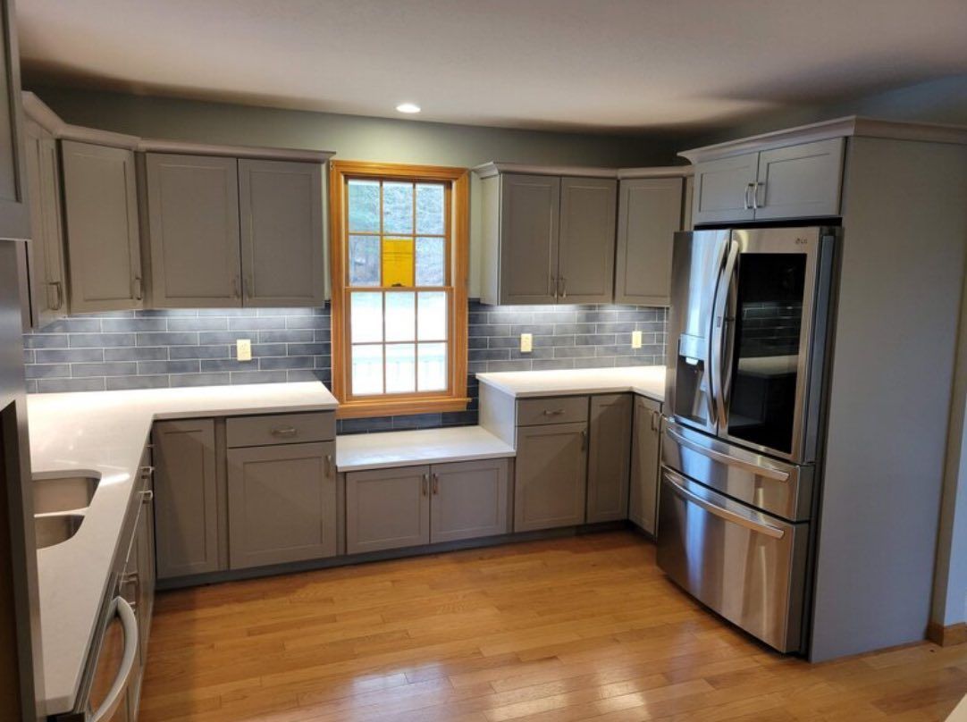 Gray kitchen with white countertops, wooden floors, and stainless steel refrigerator.