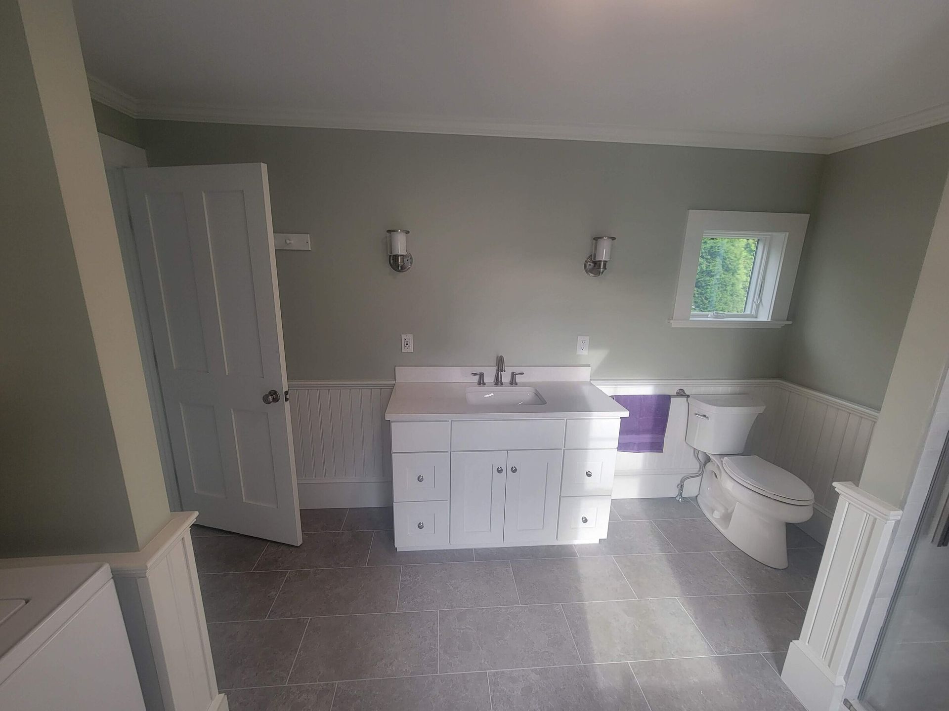 Bathroom with white vanity, toilet, and a window. Pale green walls and white trim.