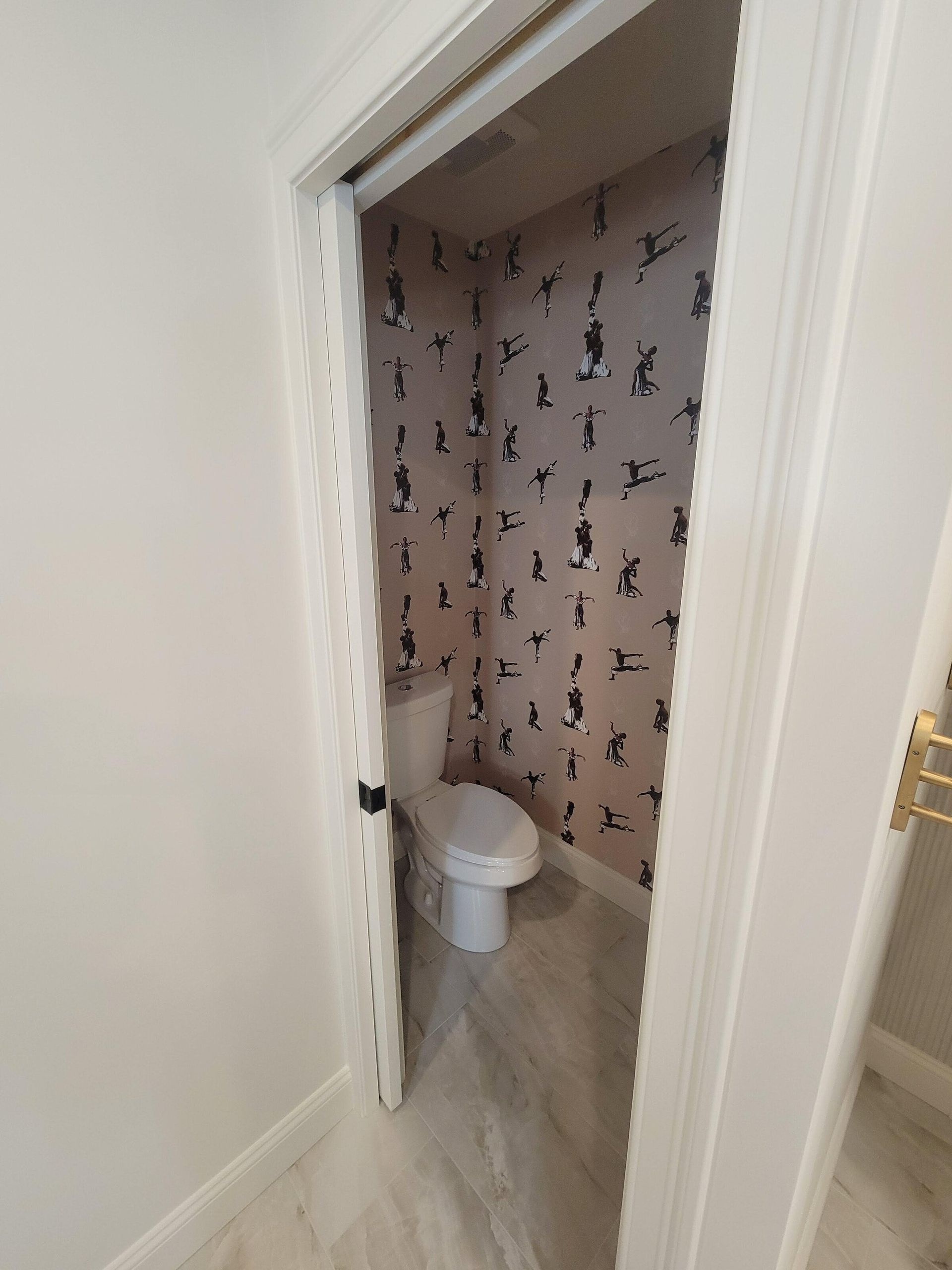 Small powder room with gray patterned wallpaper, white toilet, and marble-look floor.