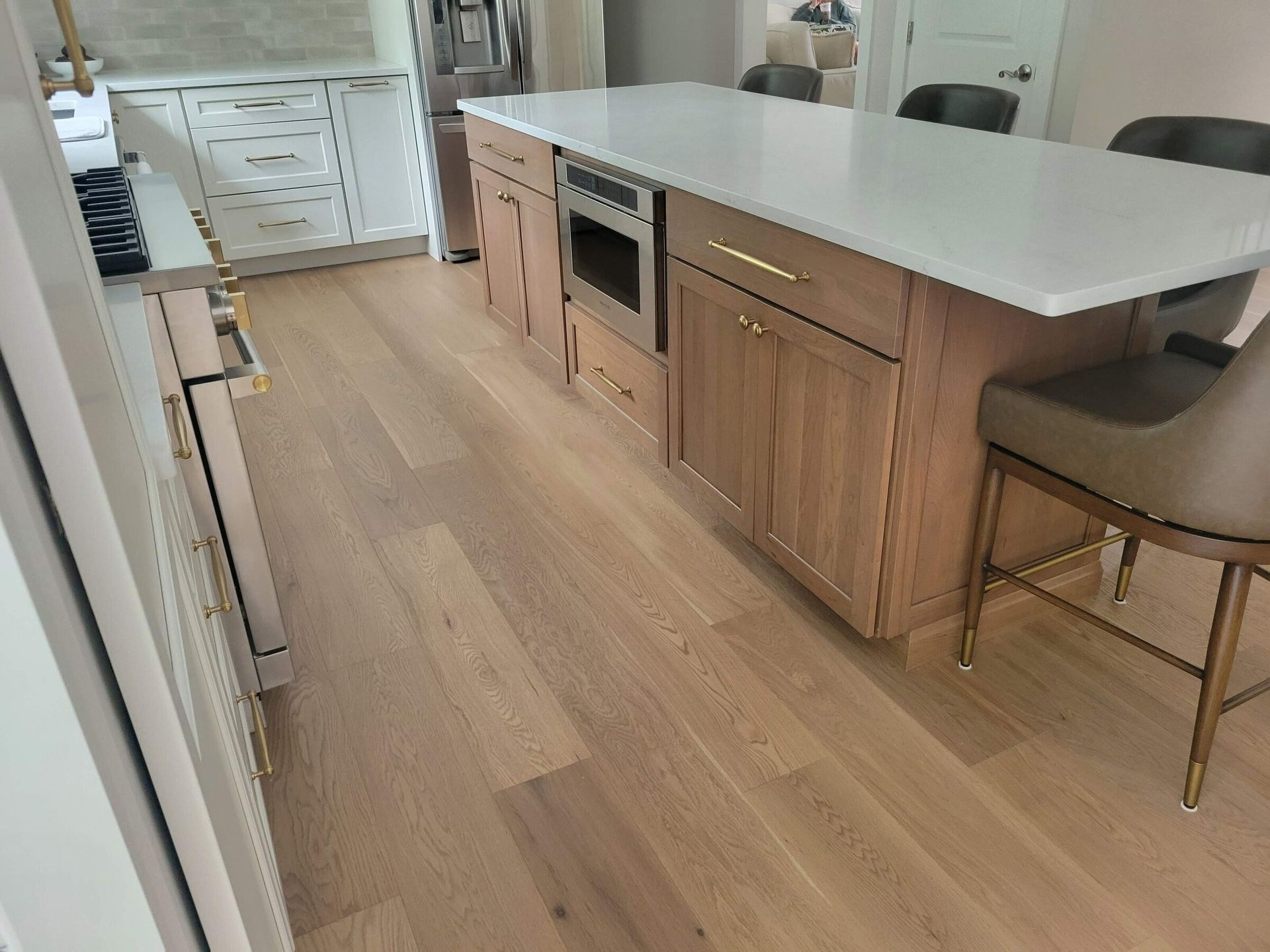 Kitchen with light wood floor, island with a white countertop, wooden cabinets, and a built-in microwave.