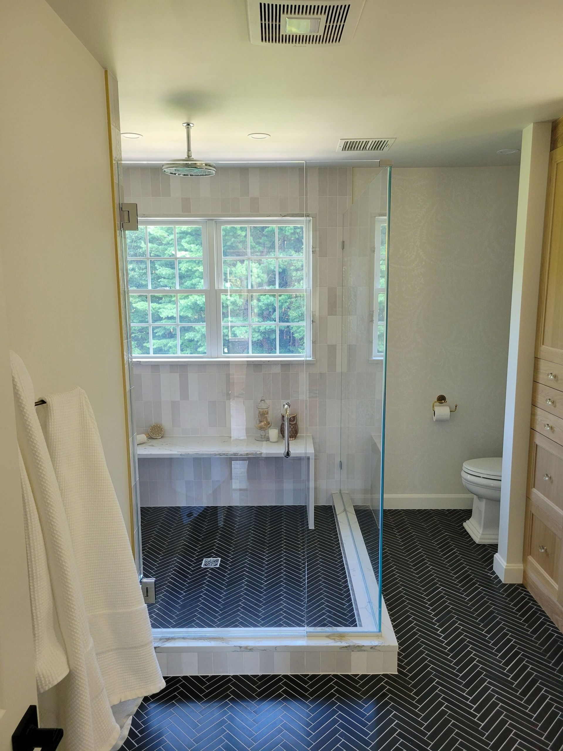 Modern bathroom with a glass shower, white walls, black and white patterned tile flooring, and a toilet.
