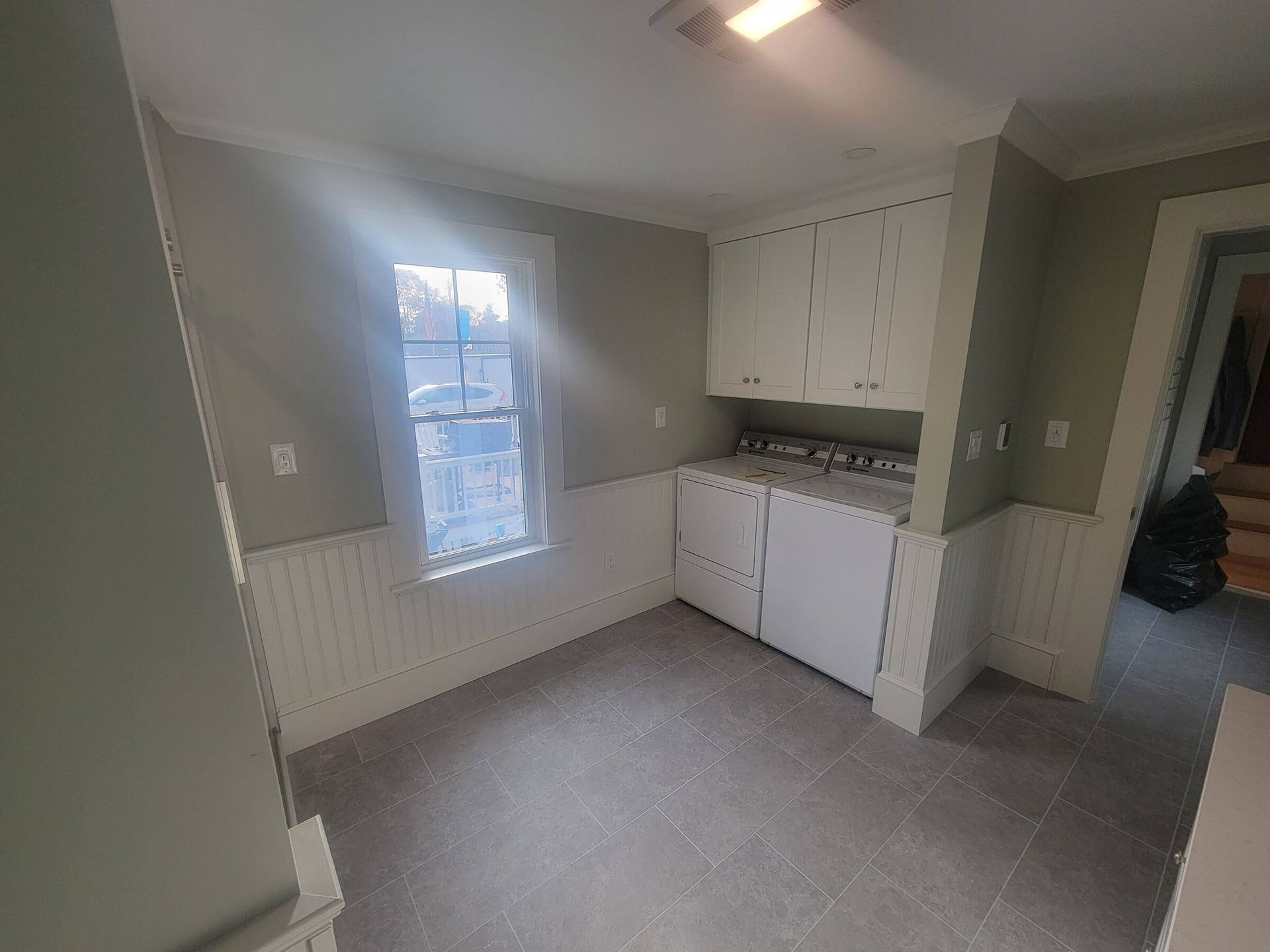 Small room with white cabinets, wainscoting, a window, and gray flooring.