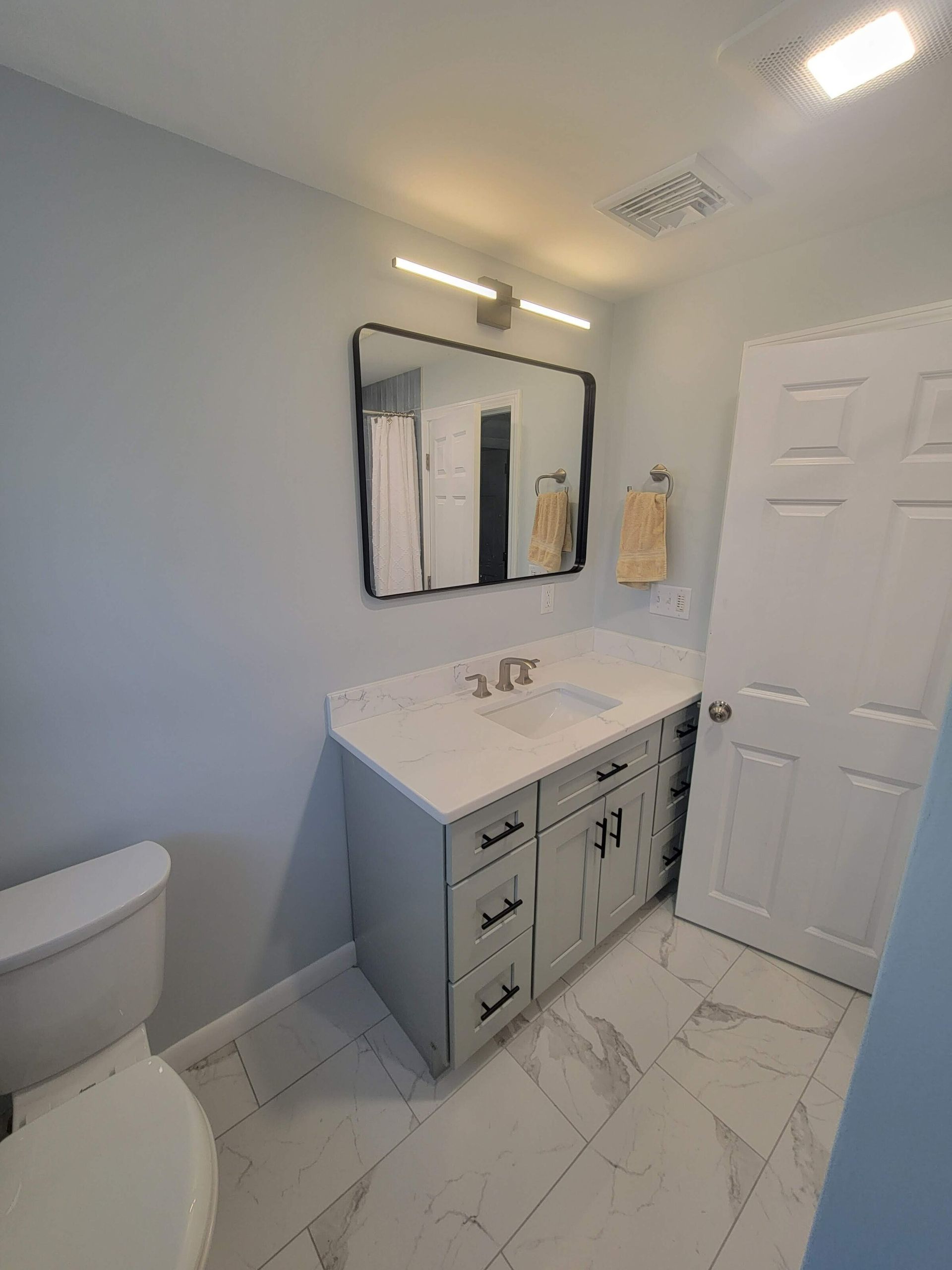 Bathroom with gray vanity, rectangular mirror, white door, and marble-look tile flooring.