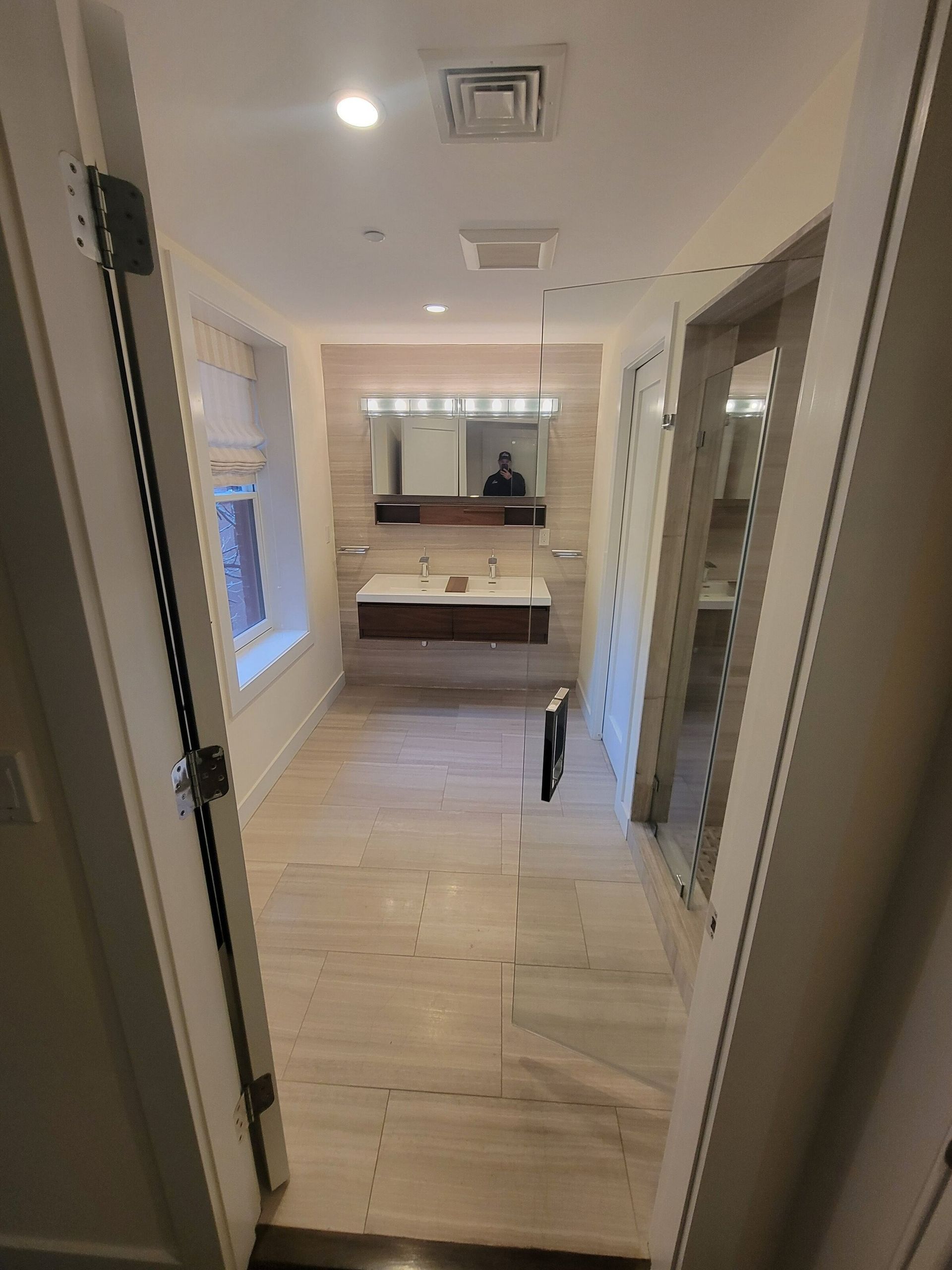 Bathroom with a floating vanity, tiled walls, a glass shower door, and beige flooring.