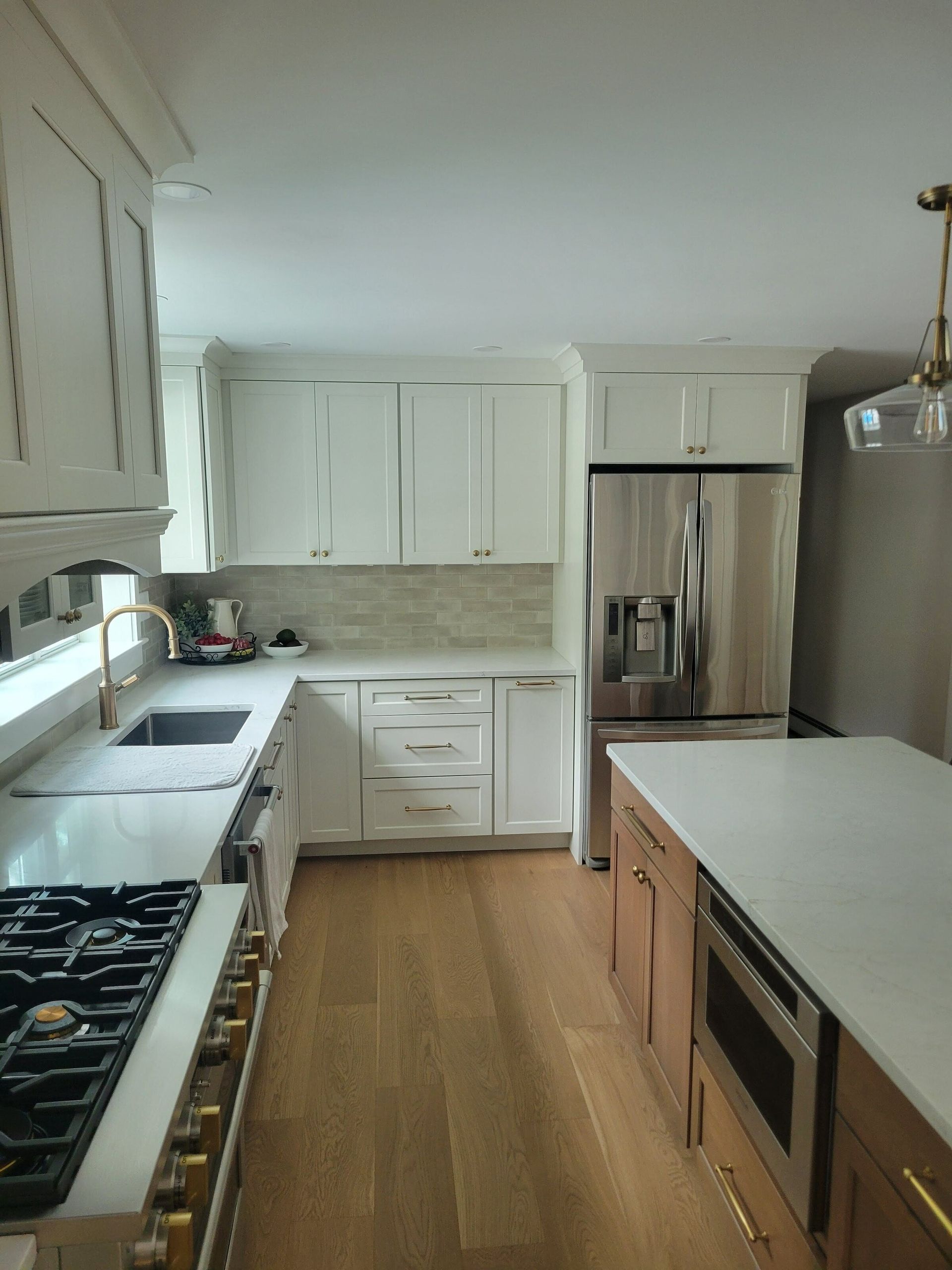 White kitchen with stainless steel refrigerator, wooden island, and gas stove.