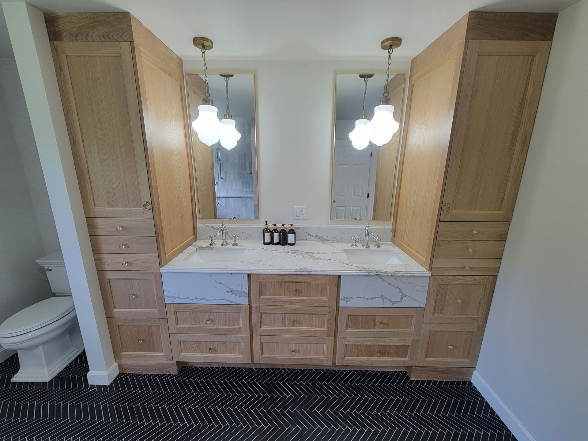 Bathroom vanity with light wood cabinets, mirrors, and patterned floor.