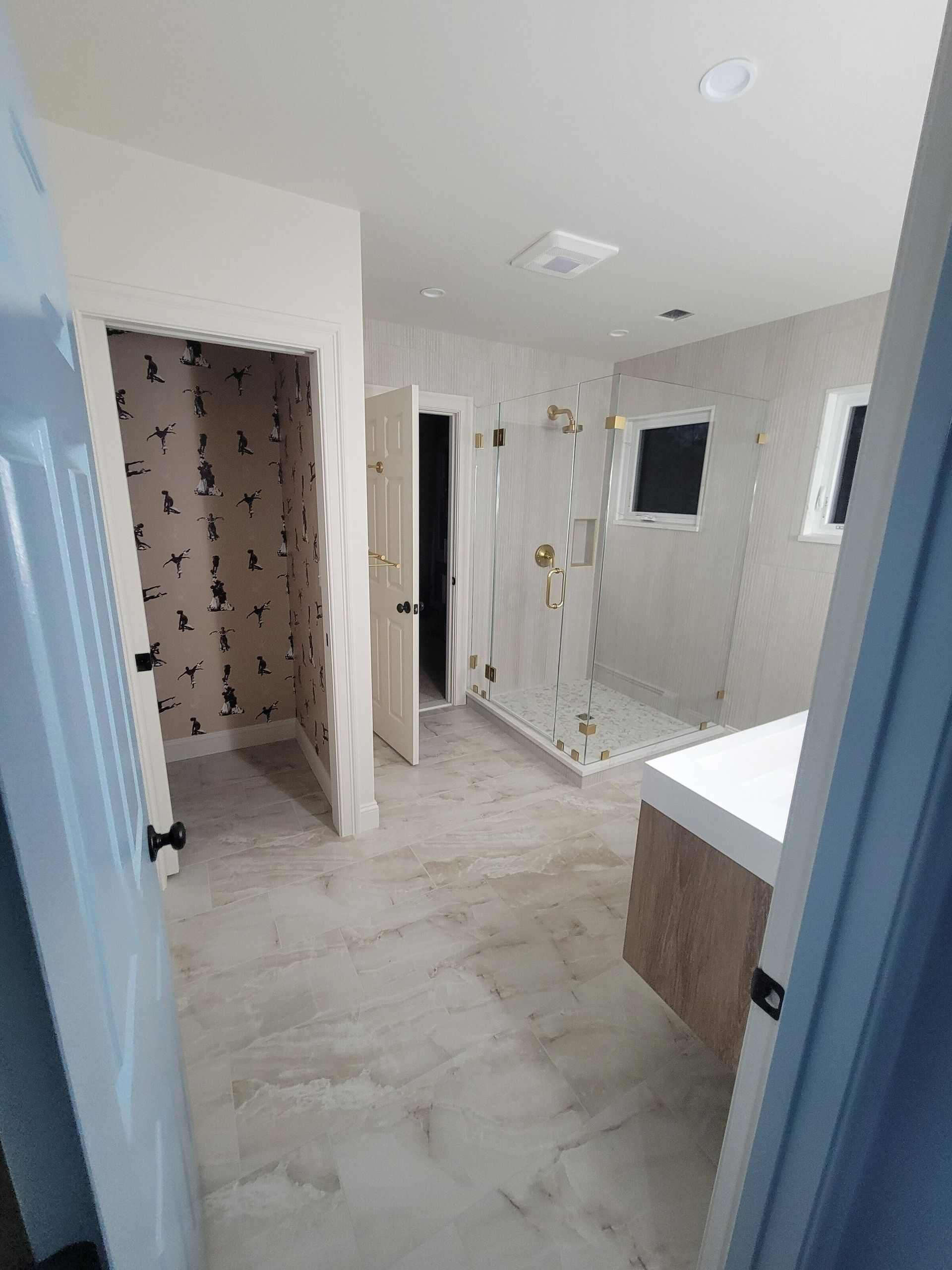 Bathroom interior with open doorways, shower, vanity, and neutral-toned tiled floor.